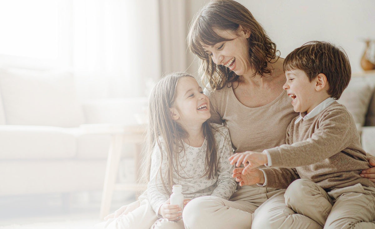 Mother and two young children laughing together on a living room floor